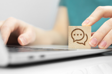 A person using a computer with a wood block featuring a text bubble