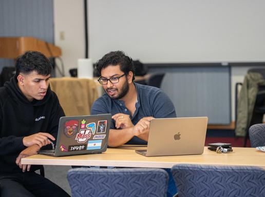 Two students consult their laptops side-by-side while participating in a cybersecurity hackathon event.