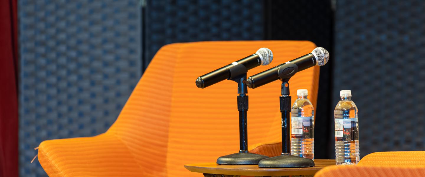 Two waiting microphones sitting on stage with chairs