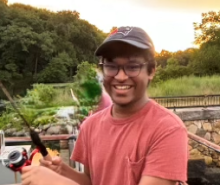 Young man wearing baseball cap and holding fishing rod, smiling at camera